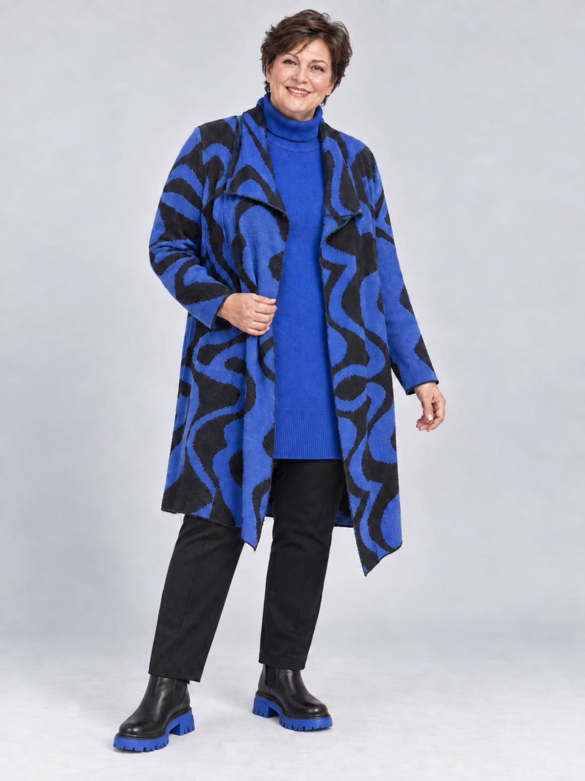Offene royalblaue Strickjacke mit geschwungenem Muster, getragen zu blauem Rollkragenpulli